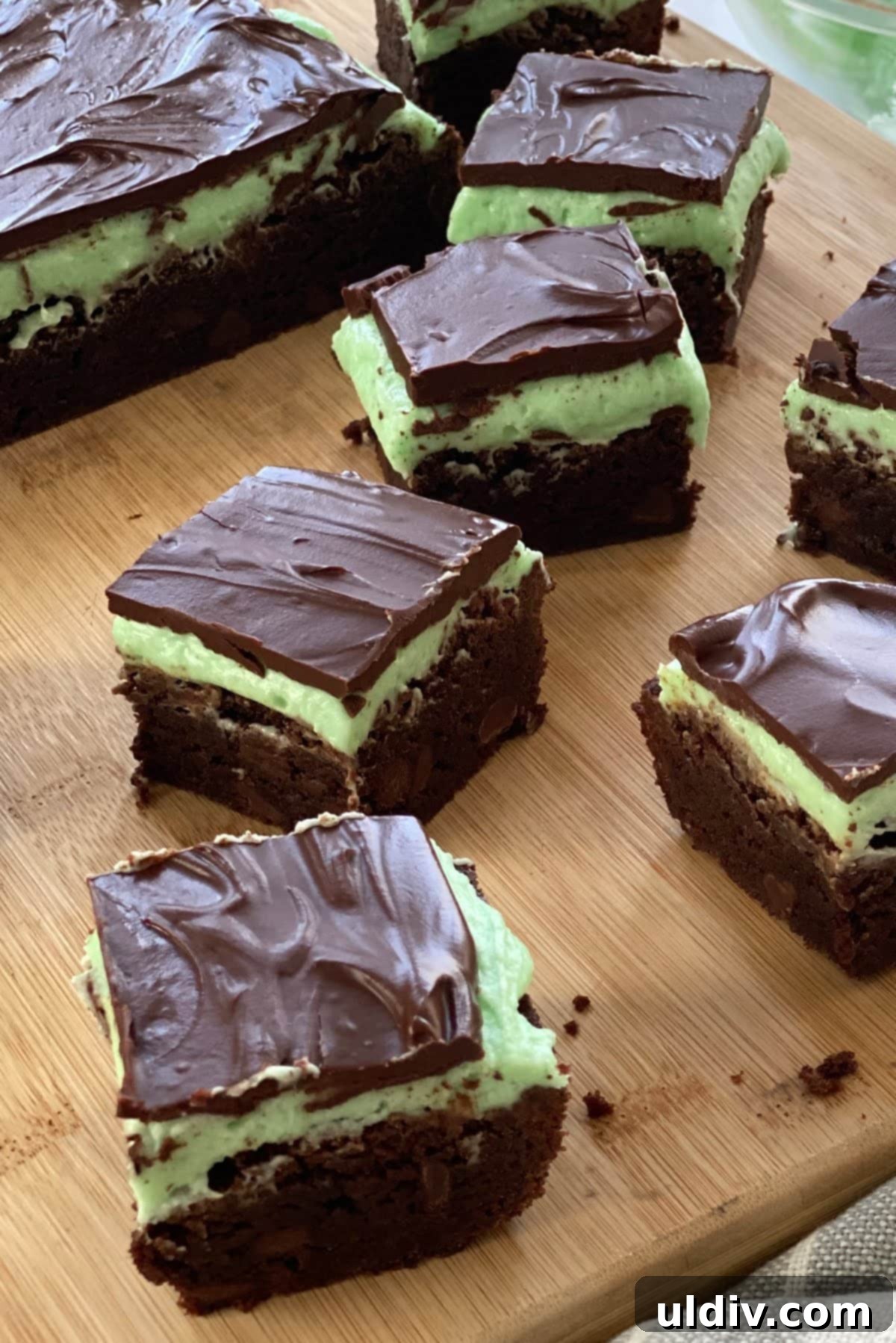 Sinfully Fudgy Mint Brownies 2 Decadent Mint Brownies with green mint buttercream and chocolate fudge topping on a cutting board, ready to be served.