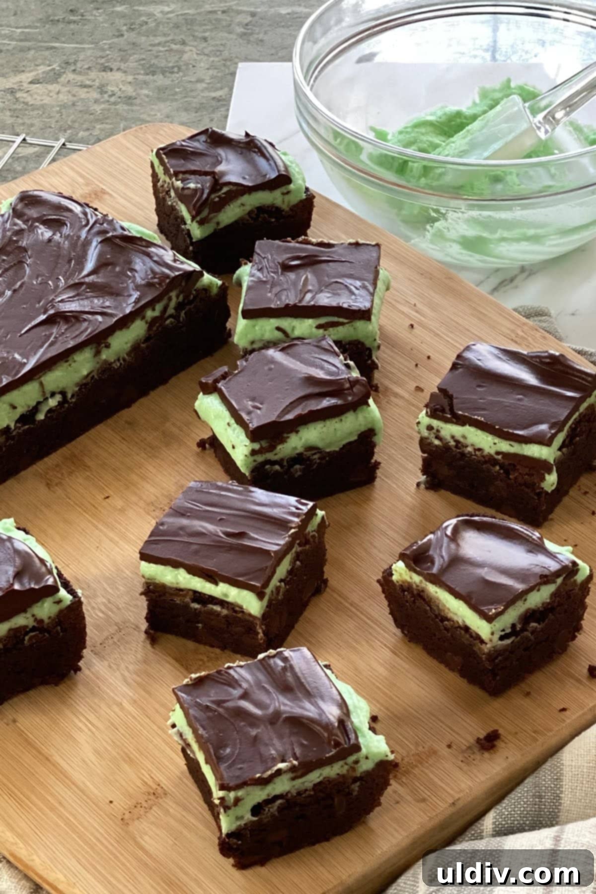 Sinfully Fudgy Mint Brownies 5 Six perfectly cut mint brownies with distinct green and brown layers, arranged on a rustic wooden cutting board.