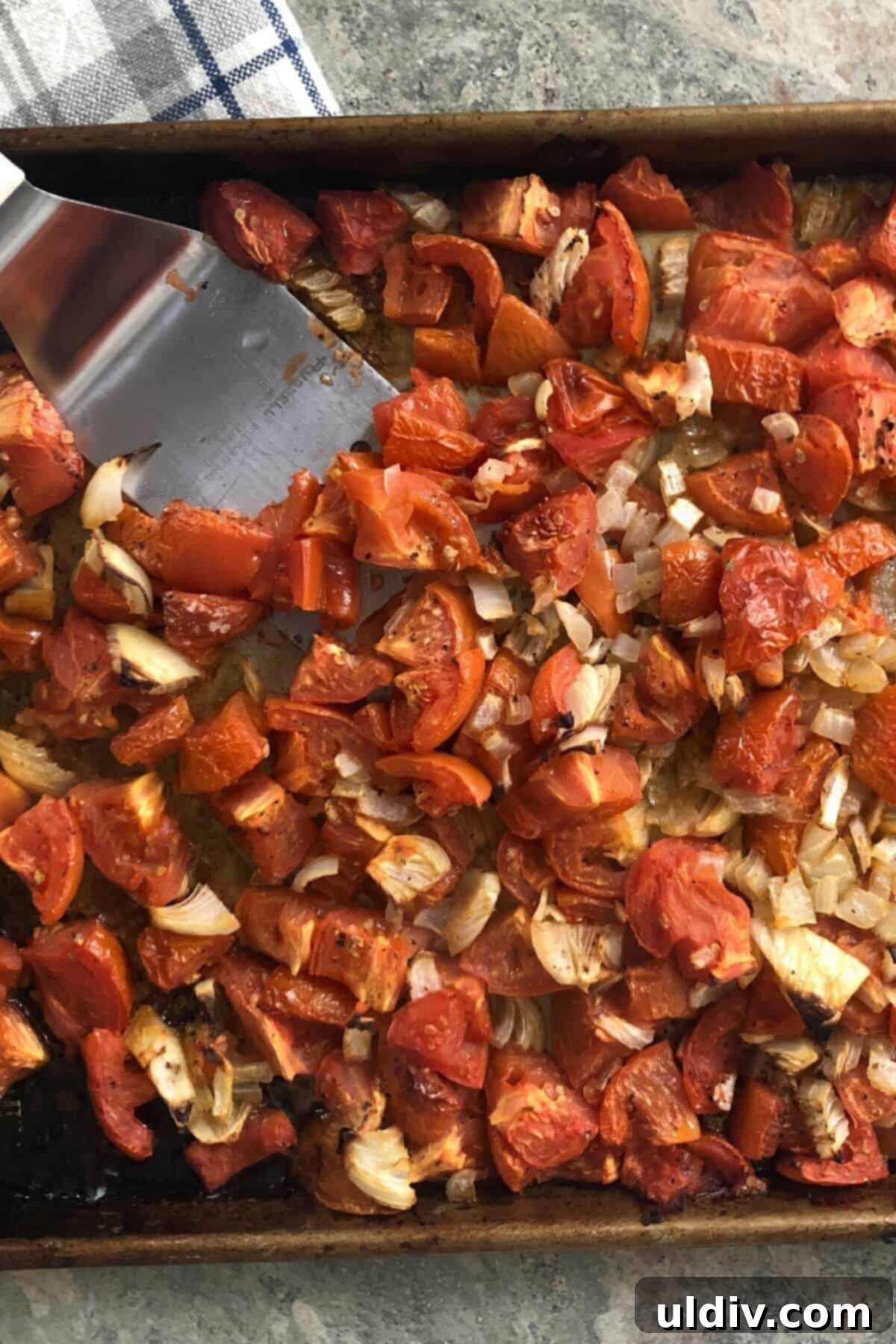Velvety Tomato Basil Bisque 6 A large metal spatula gently stirring perfectly roasted tomatoes, onions, and garlic on a baking pan, showing their caramelized edges and softened texture after oven roasting.