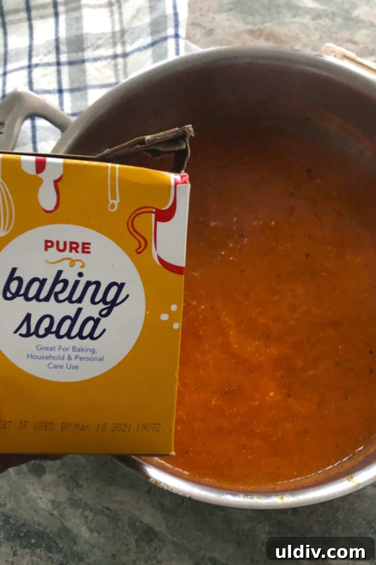 Velvety Tomato Basil Bisque 7 A person's hand adding a tiny pinch of white baking soda into a pot of simmering red tomato soup to neutralize acidity.