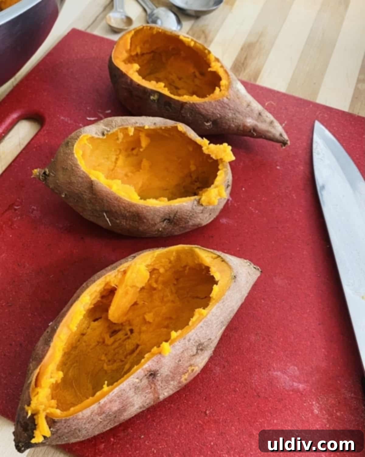 Baked sweet potatoes with their tops sliced off and the creamy orange flesh scooped out, ready for mashing.