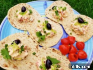 A plate of freshly prepared Flatout Foldit sandwiches, filled with cream cheese and vibrant roasted red pepper mixture, garnished with fresh green onions and olives.