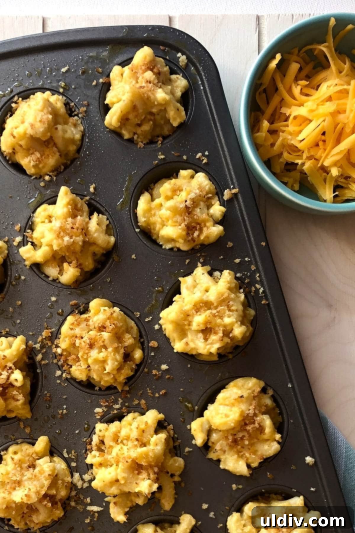 Crispy Mac & Cheese Bites: The Ultimate Kid & Party Treat 3 A mini muffin pan filled with unbaked mac and cheese bites, with a generous sprinkle of shredded cheese on top.