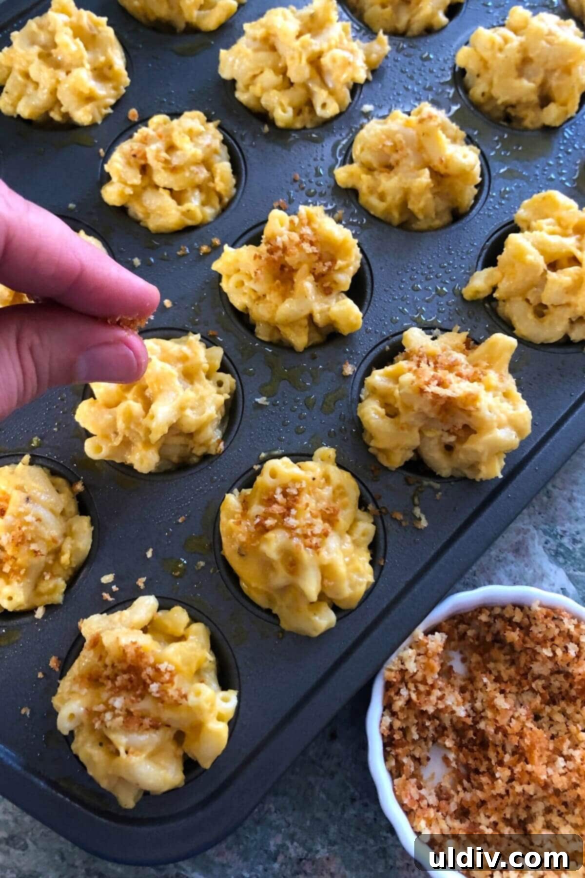 Crispy Mac & Cheese Bites: The Ultimate Kid & Party Treat 9 Golden toasted panko breadcrumbs being sprinkled over mini mac and cheese bites in a muffin pan, adding a crispy topping.