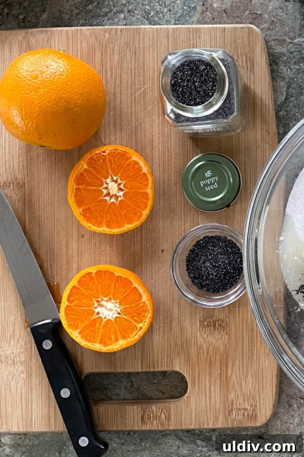 Sunshine Orange Poppy Muffins 5 A whole orange, a halved orange, and a bowl of poppy seeds on a wooden board.