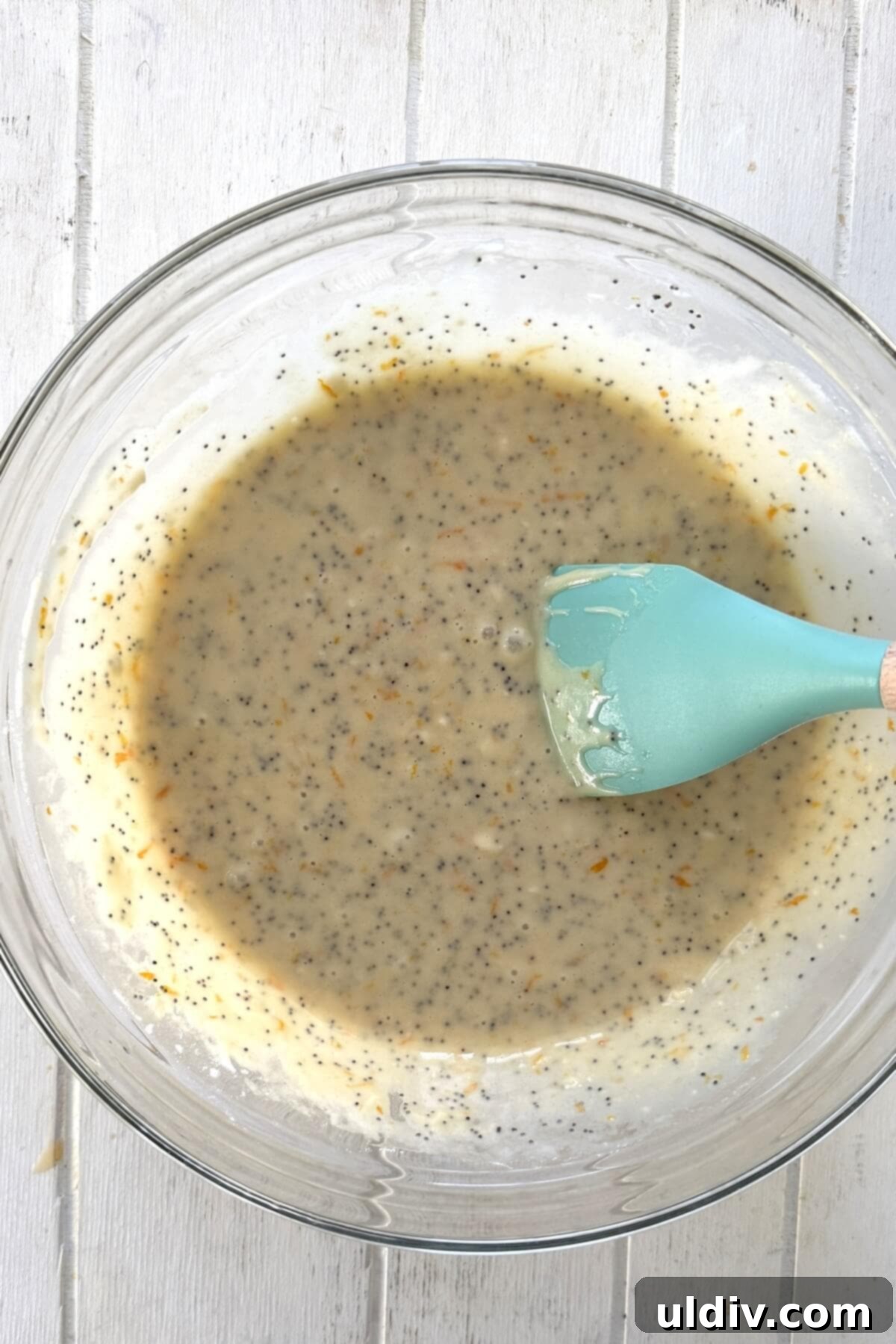 Sunshine Orange Poppy Seed Glaze Muffins 7 Muffin batter is gently mixed with a spatula in a bowl, showing the consistency.