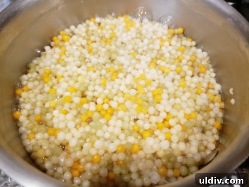 Evdeki Malzemelerle Yazlık Vegan Kuskus Salatası 5 Cooked tricolor pearl couscous in a mixing bowl, ready for additions.