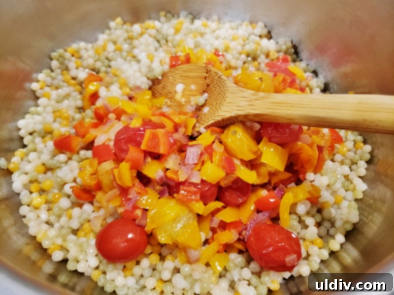 Evdeki Malzemelerle Yazlık Vegan Kuskus Salatası 6 Sautéed vegetables being added to the cooked couscous in a large bowl.