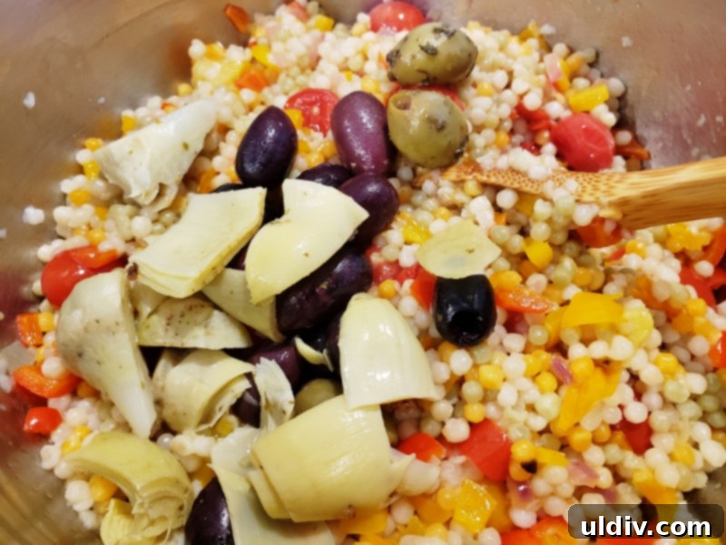 Evdeki Malzemelerle Yazlık Vegan Kuskus Salatası 8 Artichoke hearts and green and black olives being added to the couscous and vegetable mix.