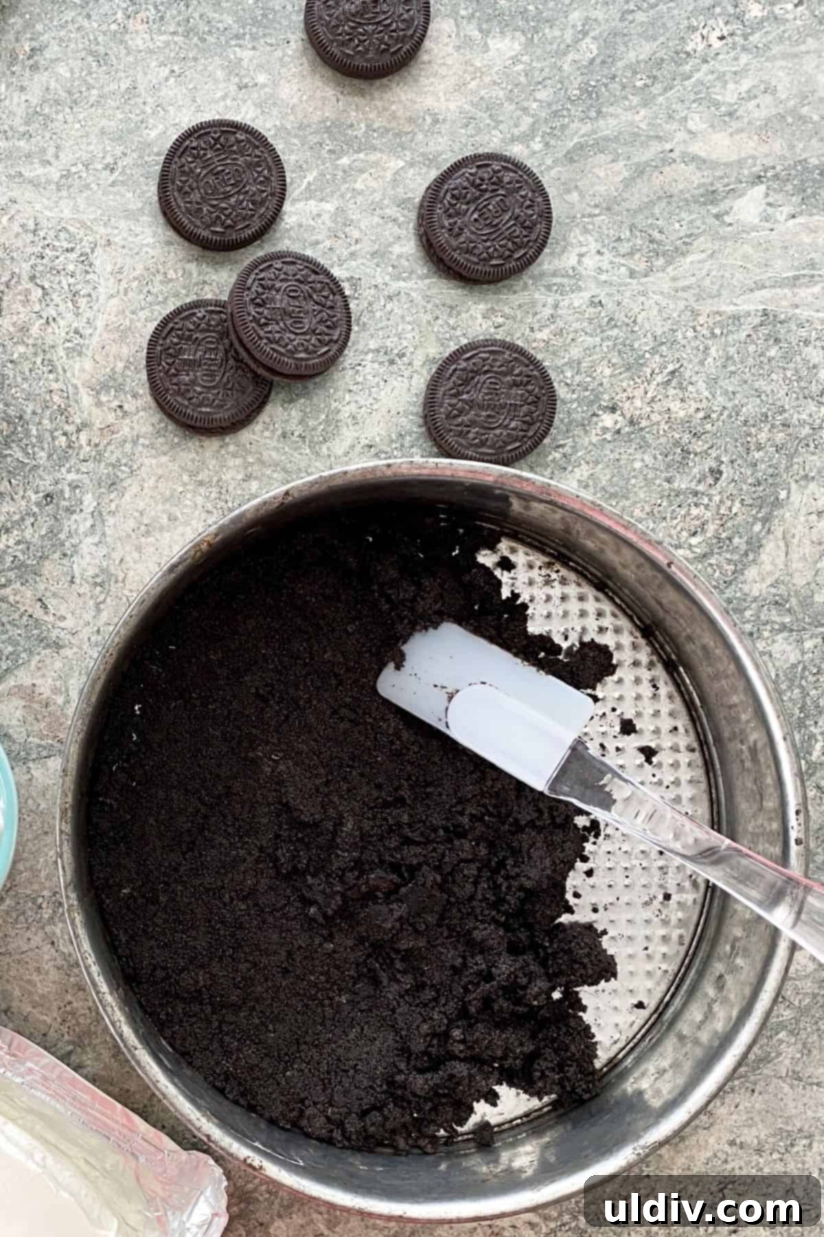 Effortless Oreo Cheesecake Recipe 12 Close-up of spreading the Oreo cookie crust mixture evenly into a springform pan with hands.