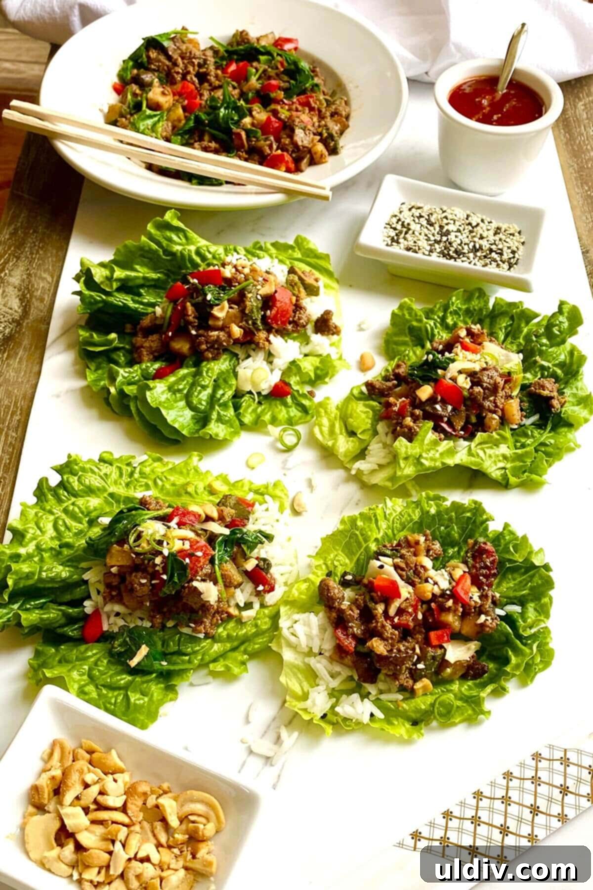 Savory Beef Lettuce Cups 5 Four perfectly assembled Korean beef lettuce wraps, garnished with sesame seeds and green onions on a platter.