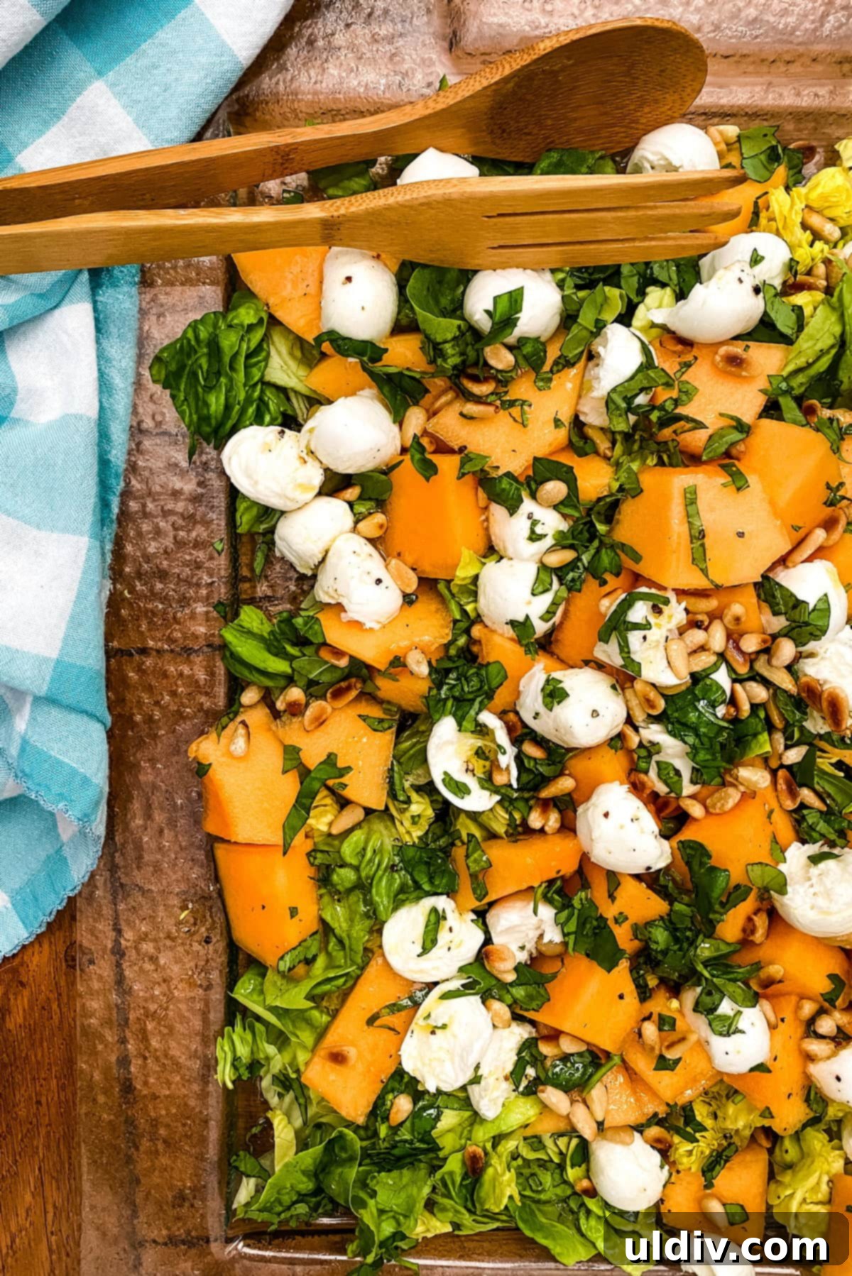 A vibrant glass platter showcasing a refreshing melon salad with cantaloupe, fresh mozzarella, and pine nuts, dressed with a lemon honey vinaigrette.