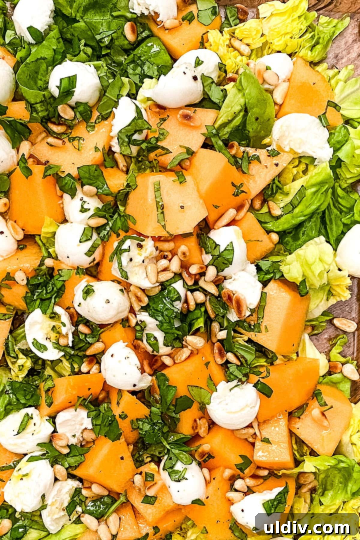 Close-up of a refreshing melon salad featuring cantaloupe, creamy fresh mozzarella, and toasted pine nuts, perfect for summer.