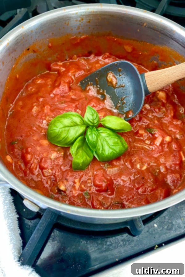 Signature Fresh Basil Marinara 2 A pot of rich red marinara sauce, garnished with a sprig of fresh green basil, ready to be served or stored.