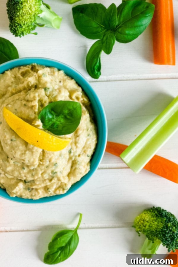 Vibrant Basil Hummus 4 A close-up shot of a bowl of creamy basil hummus, perfectly garnished with a fresh basil leaf and a lemon wedge, surrounded by crisp celery and carrot sticks, inviting a delicious dip.