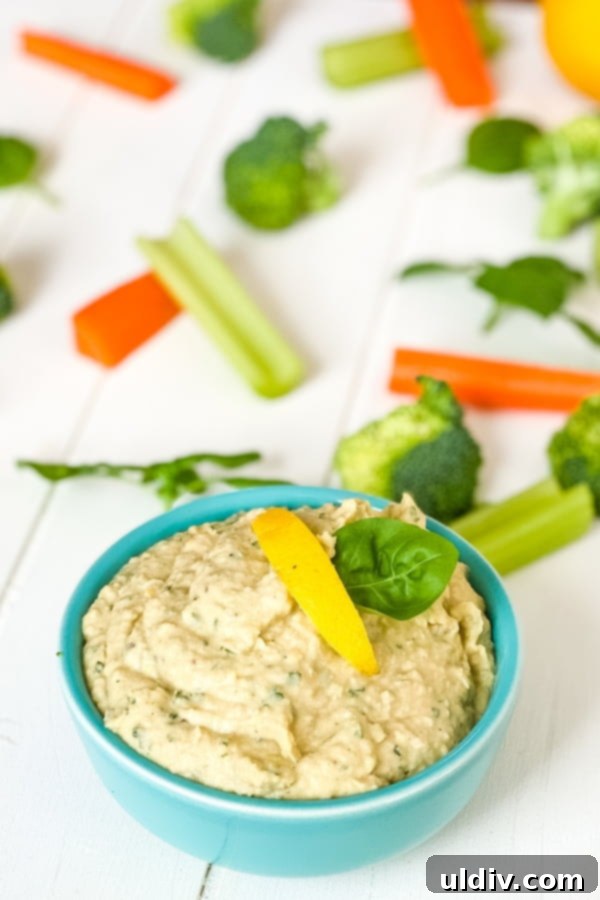 Vibrant Basil Hummus 5 A close-up of basil hummus served in a rustic bowl, garnished with fresh herbs and a drizzle of olive oil, accompanied by an assortment of colorful dippers including crunchy carrots, crisp celery, and vibrant broccoli florets.