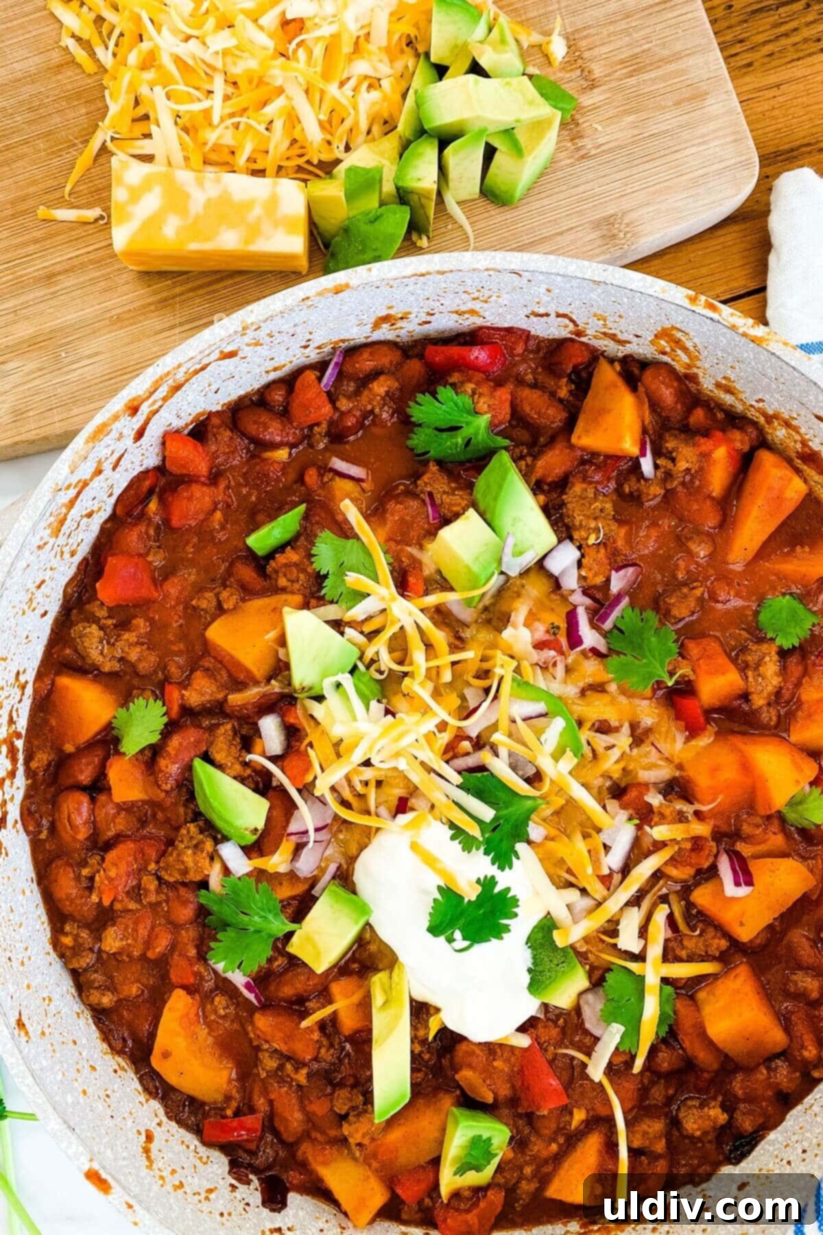 Beef and butternut squash chili in a pot topped with avocado, cheese and sour cream.
