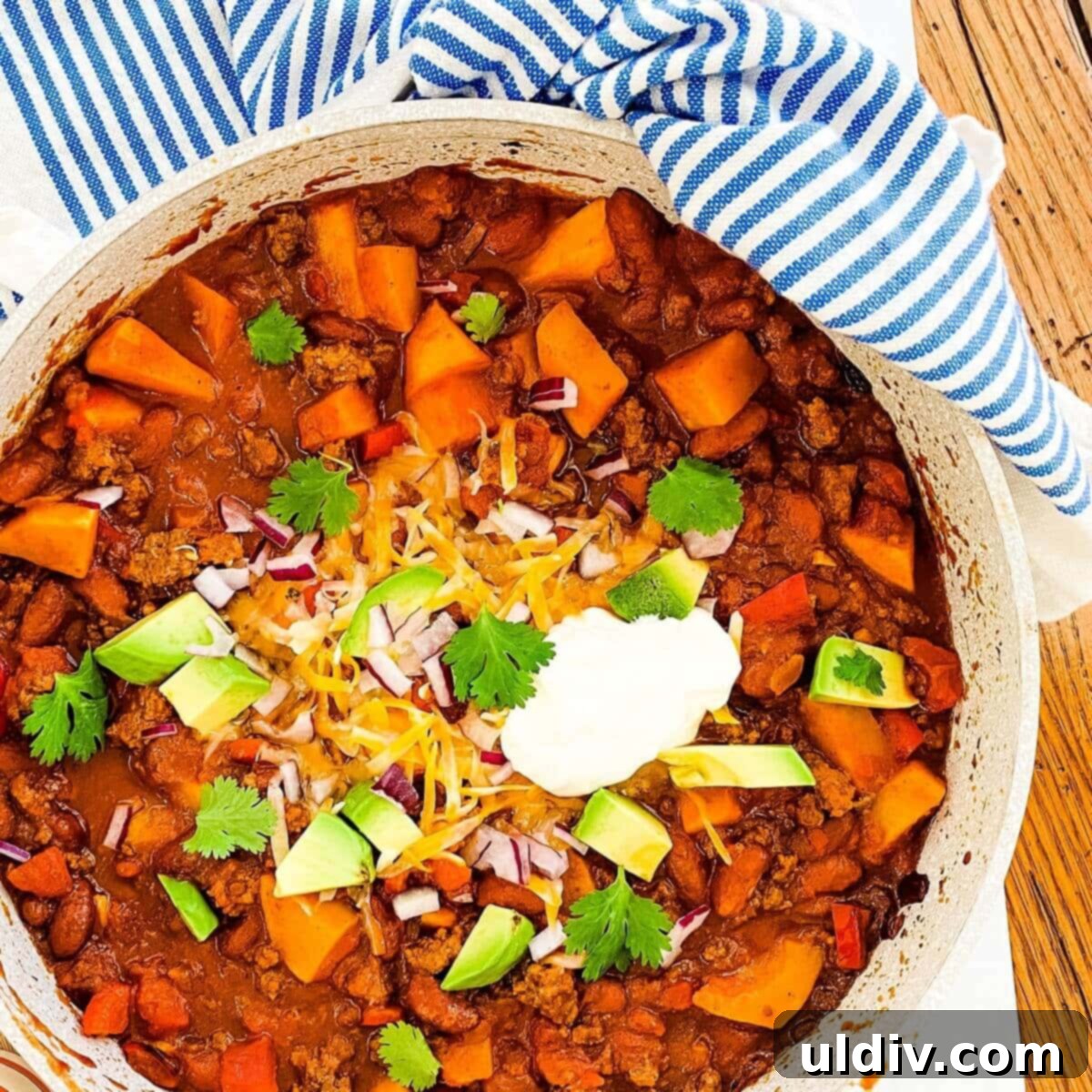 Ground beef and butternut squash chili in a large pot topped with cheese, avocado, sour cream, and cilantro, ready to be served.