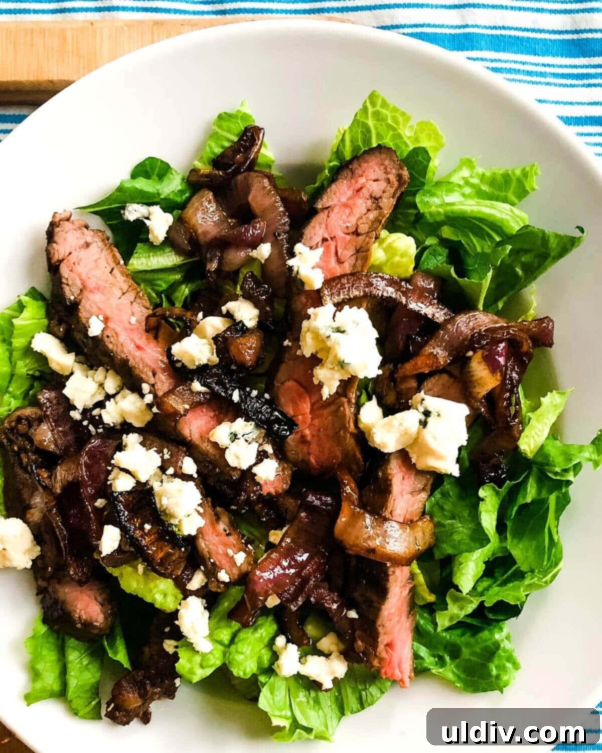 Balsamic Herb Grilled Steak Salad with Crumbled Blue Cheese 10 An elegantly plated skirt steak salad on a white plate, featuring fresh greens, sliced steak, roasted onions, and blue cheese, ready for serving.