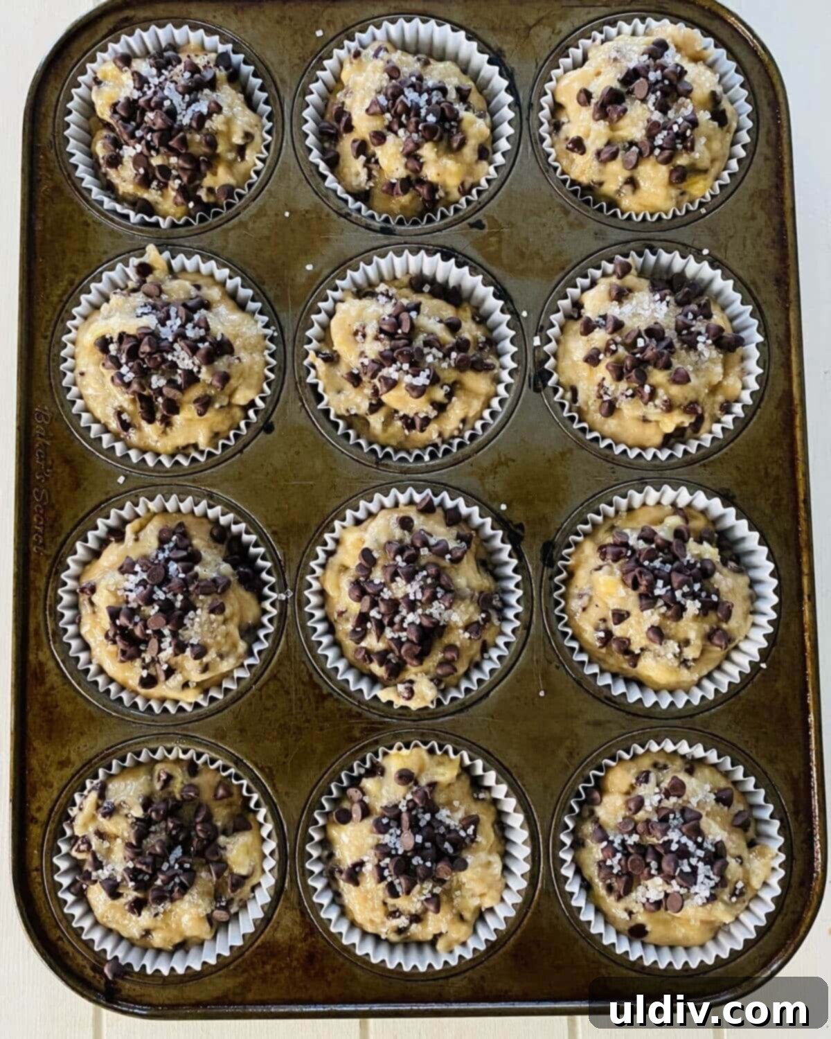 Naturally Sweet Vegan Banana Muffins 11 Unbaked dairy-free banana muffins in a lined pan, topped with extra chocolate chips and sanding sugar, ready for the oven.