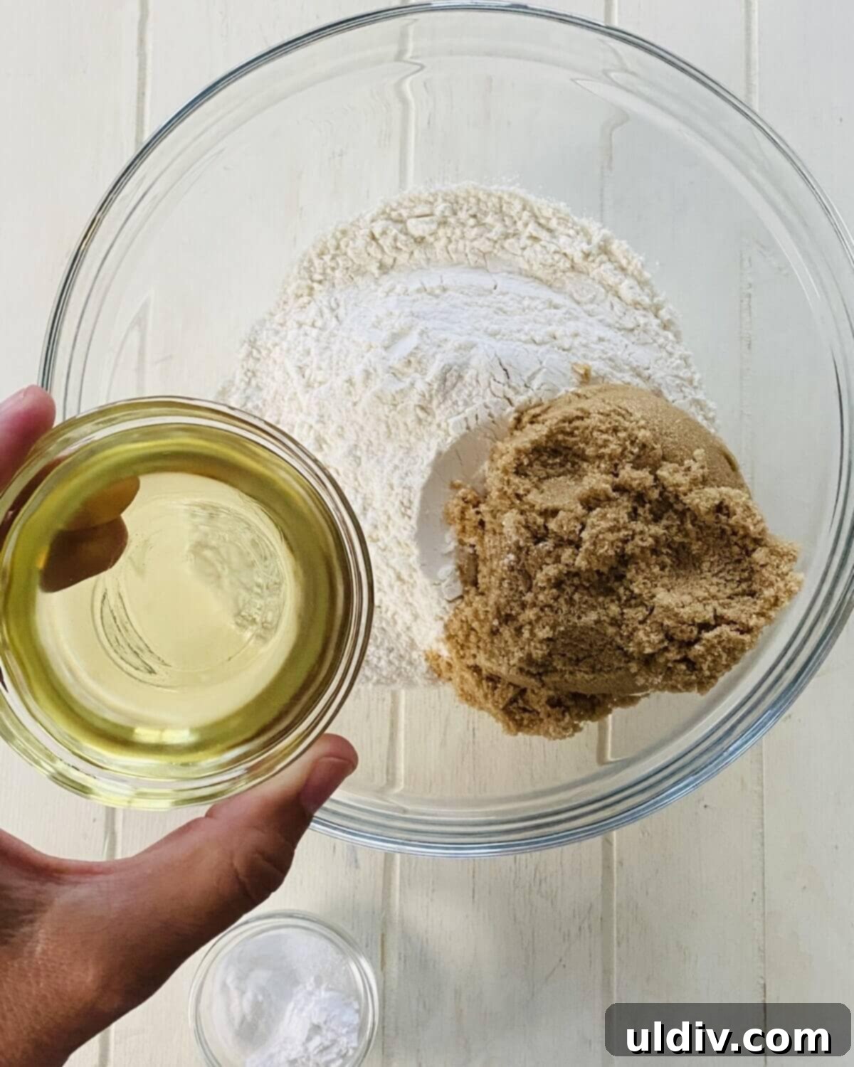 Naturally Sweet Vegan Banana Muffins 6 Adding neutral oil to a large bowl containing all-purpose flour and light brown sugar.
