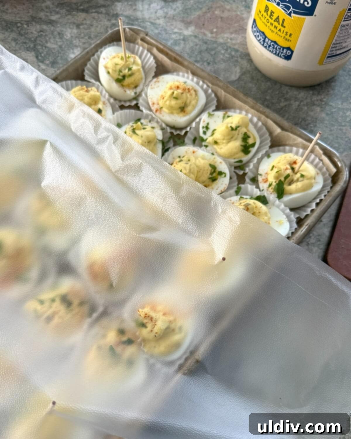 Pickle-Perfect Deviled Eggs 12 Stuffed eggs on a sheet pan with plastic wrap.