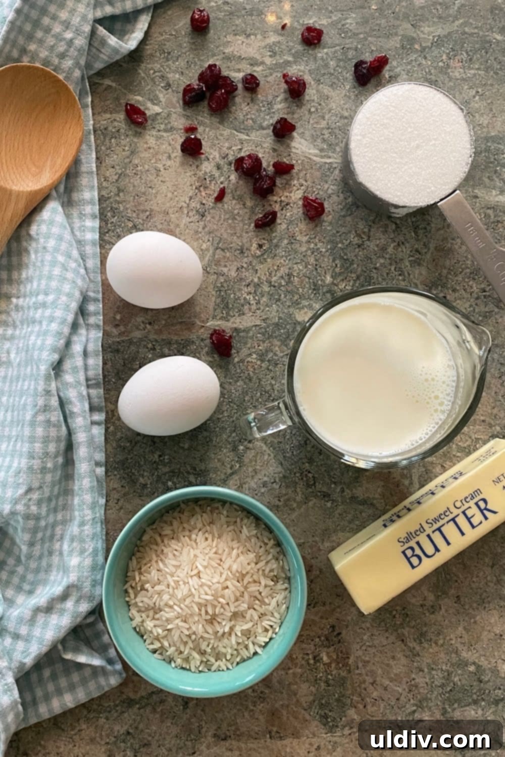 Classic Creamy Stovetop Rice Pudding 4 Essential ingredients for a creamy dessert: whole milk, long-grain rice, granulated sugar, salted butter, fresh eggs, and vibrant dried cranberries, beautifully arranged.