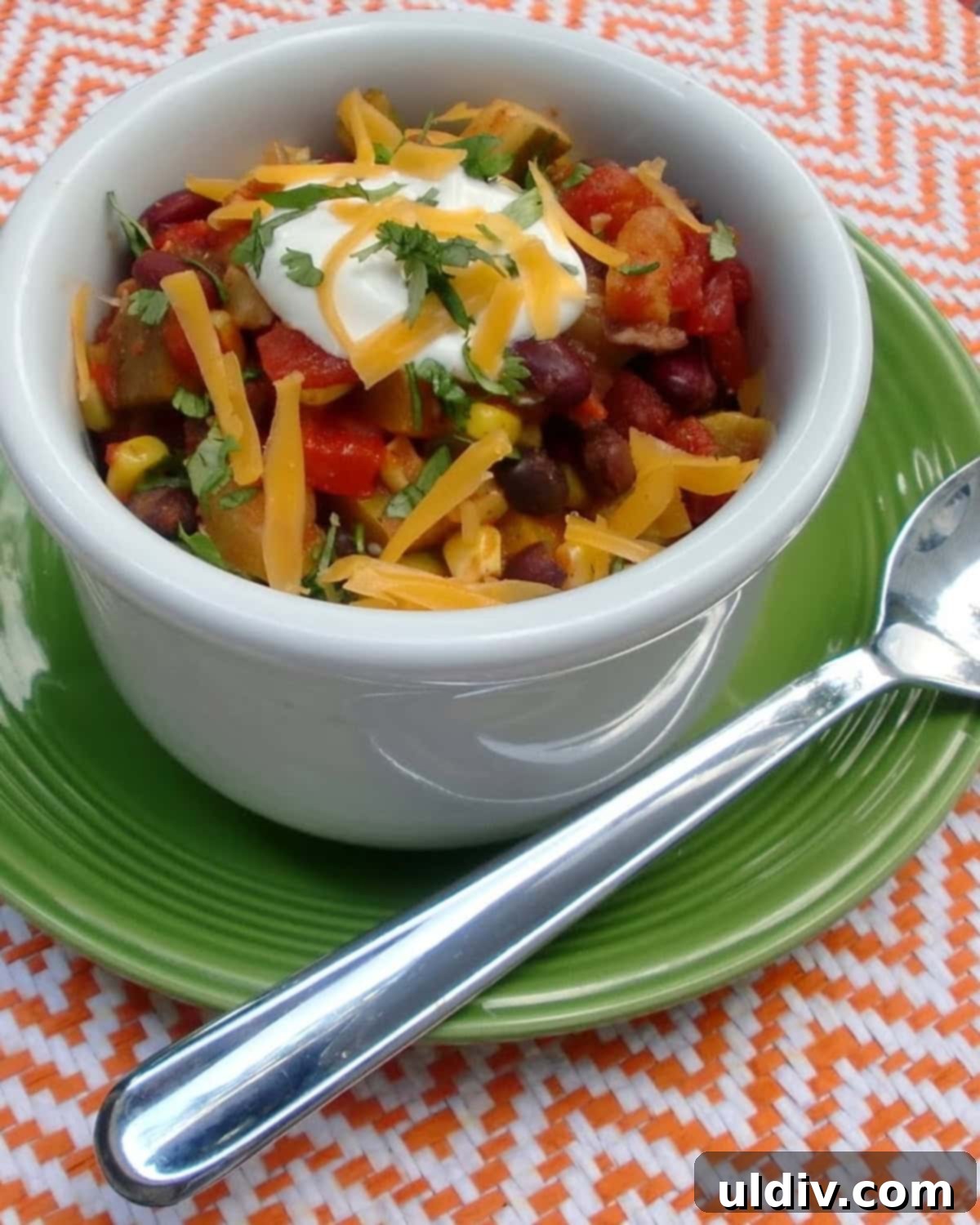 A vibrant bowl of summer vegetable chili with beans, garnished with cheese and sour cream.