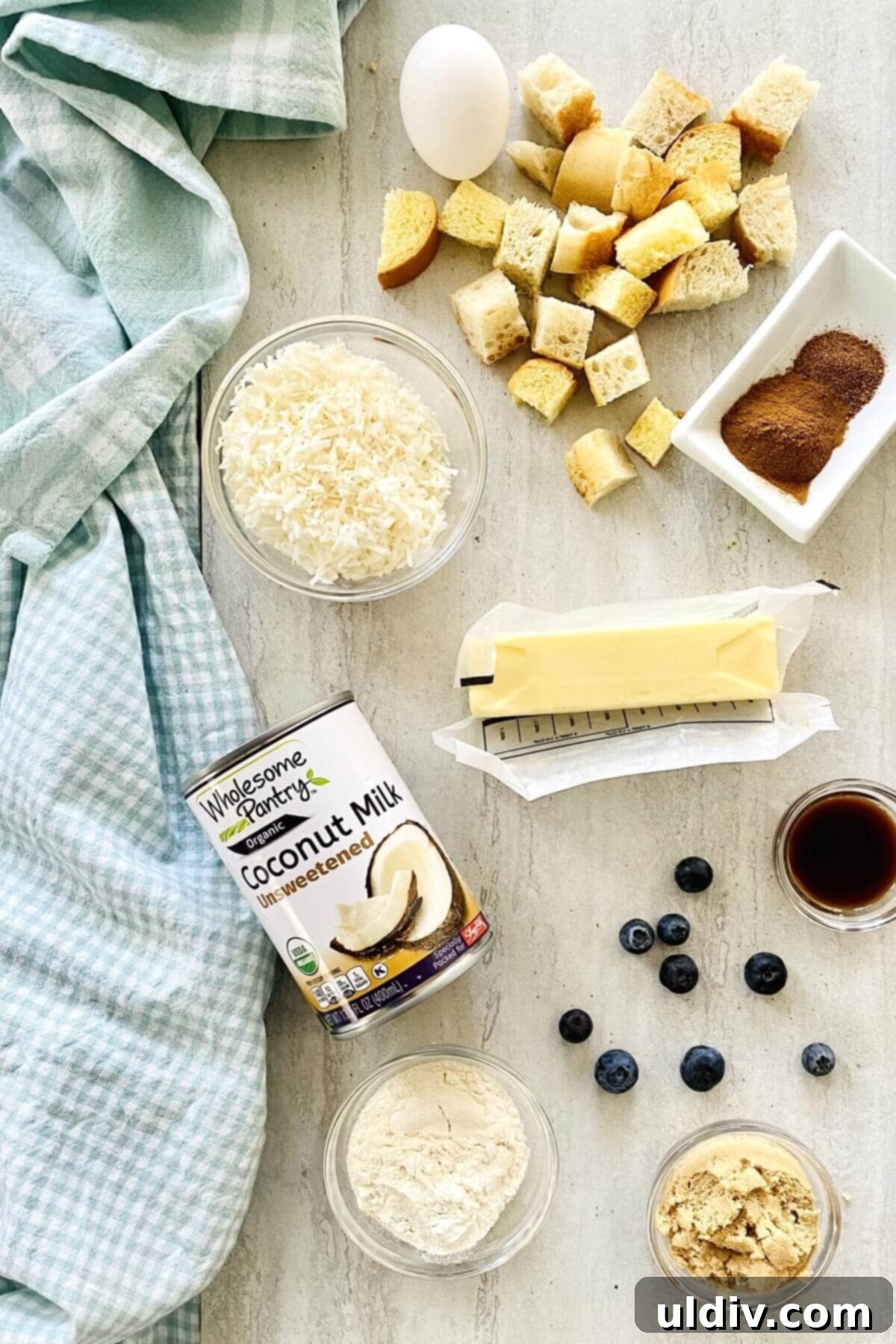 Cinnamon Coconut French Toast Muffins Bursting with Blueberries 4 Key ingredients laid out: a can of coconut milk, shredded coconut, cubes of bread, butter, and cinnamon sticks, highlighting the quality of components.