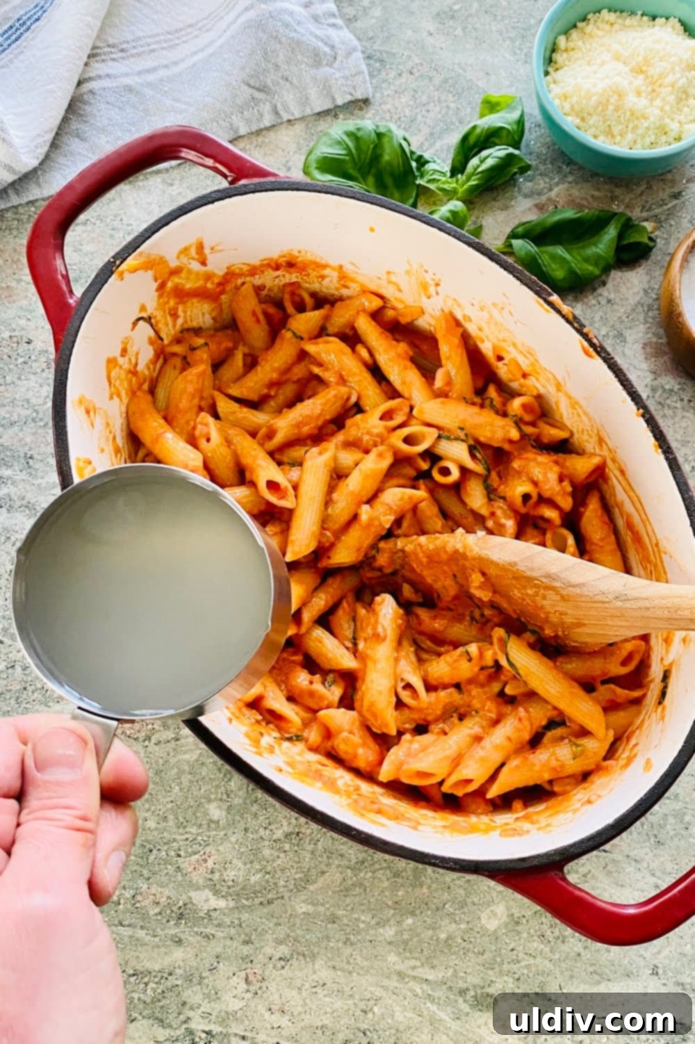Velvety Tomato Pasta 4 A chef adds a ladle of starchy pasta water to a pan of creamy tomato sauce to enhance its texture.