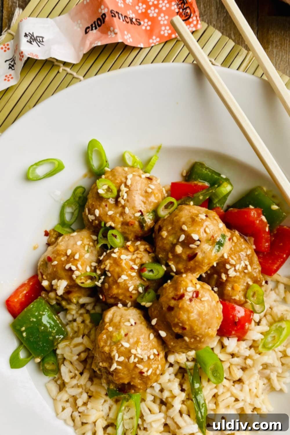 Quick-Baked Teriyaki Turkey Meatballs with a Sticky Glaze 2 A bowl of delicious teriyaki turkey meatballs served with fluffy brown rice and chopsticks, garnished with sesame seeds and green onions.