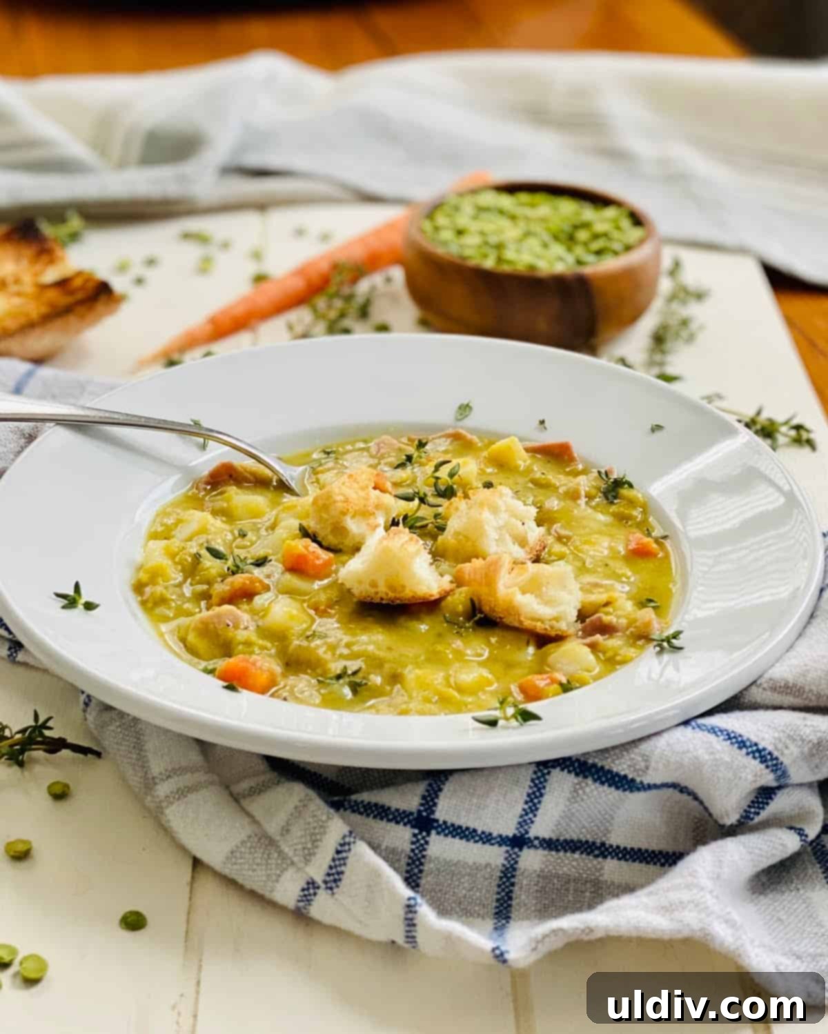 Hearty Ham and Split Pea Soup with Potatoes and Crispy Croutons 2 A bowl of split pea soup with ham and toasted croutons with a spoon in it.