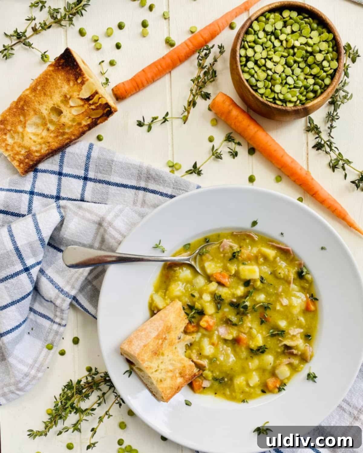Robust Ham & Potato Split Pea Soup with Crispy Croutons 4 A rustic wooden table displaying a bowl of split pea soup with ham and potatoes, alongside fresh carrots, dried split peas, and slices of artisan bread.