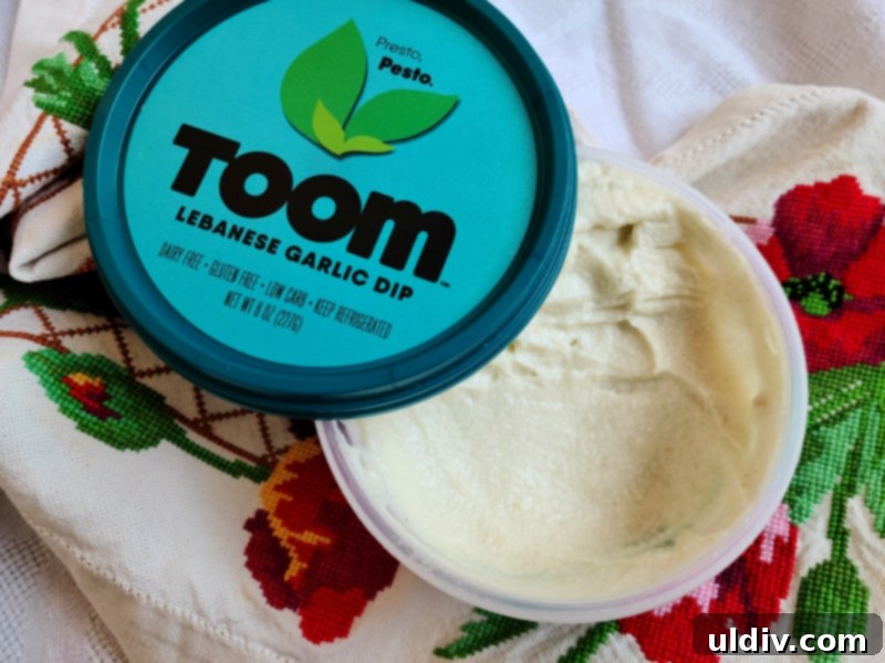 A tub of Toom Pesto dip, illustrating its vibrant green hue, surrounded by fresh herbs.