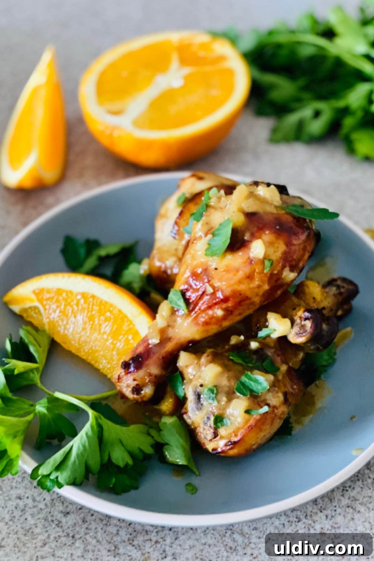 A plate featuring three perfectly oven roasted chicken legs, drizzled with a rich orange Dijon sauce, accompanied by fresh orange wedges and parsley.