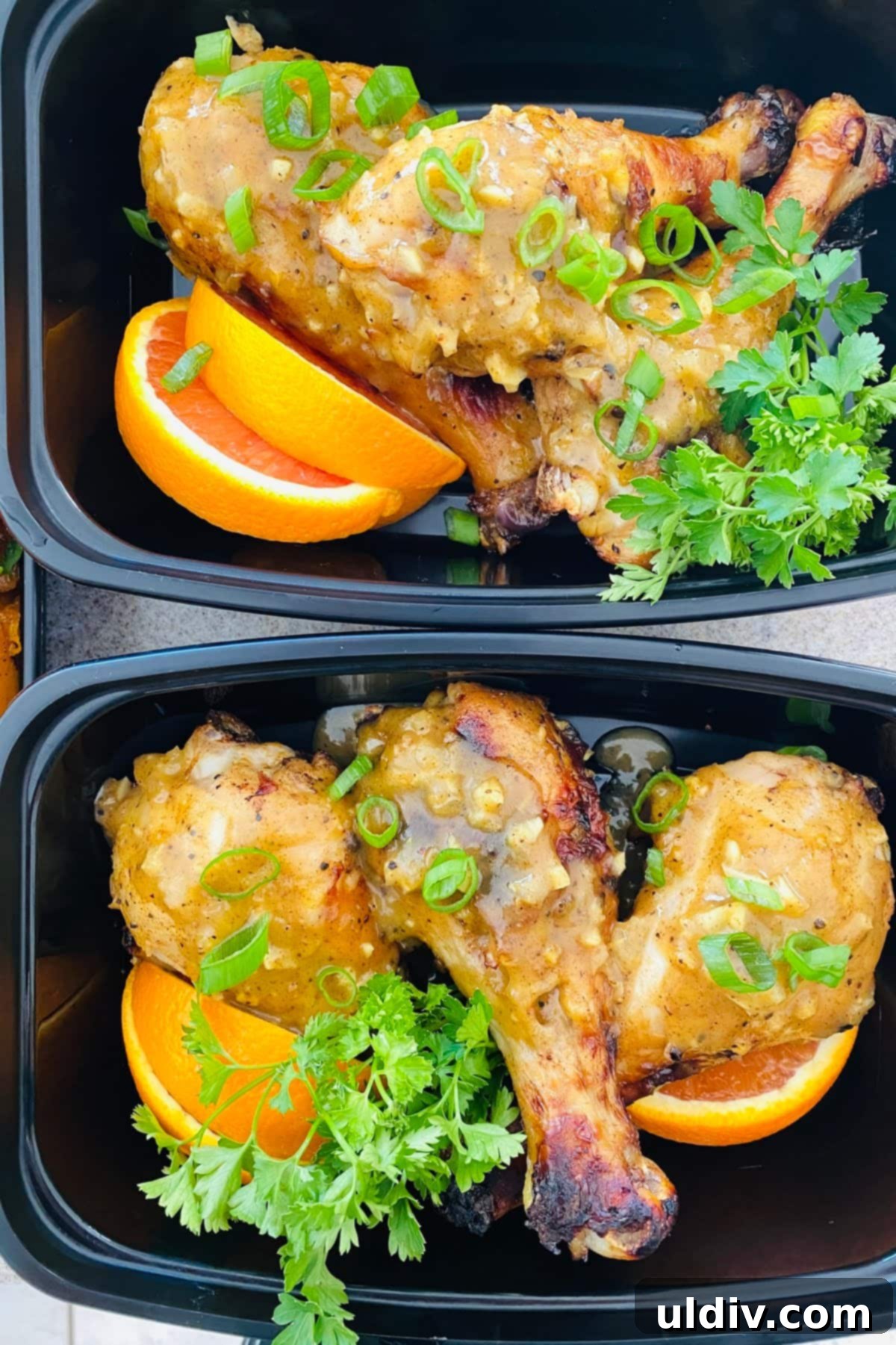 Individual portions of oven roasted chicken drumsticks with orange slices, prepared for personal chef clients in meal prep containers.