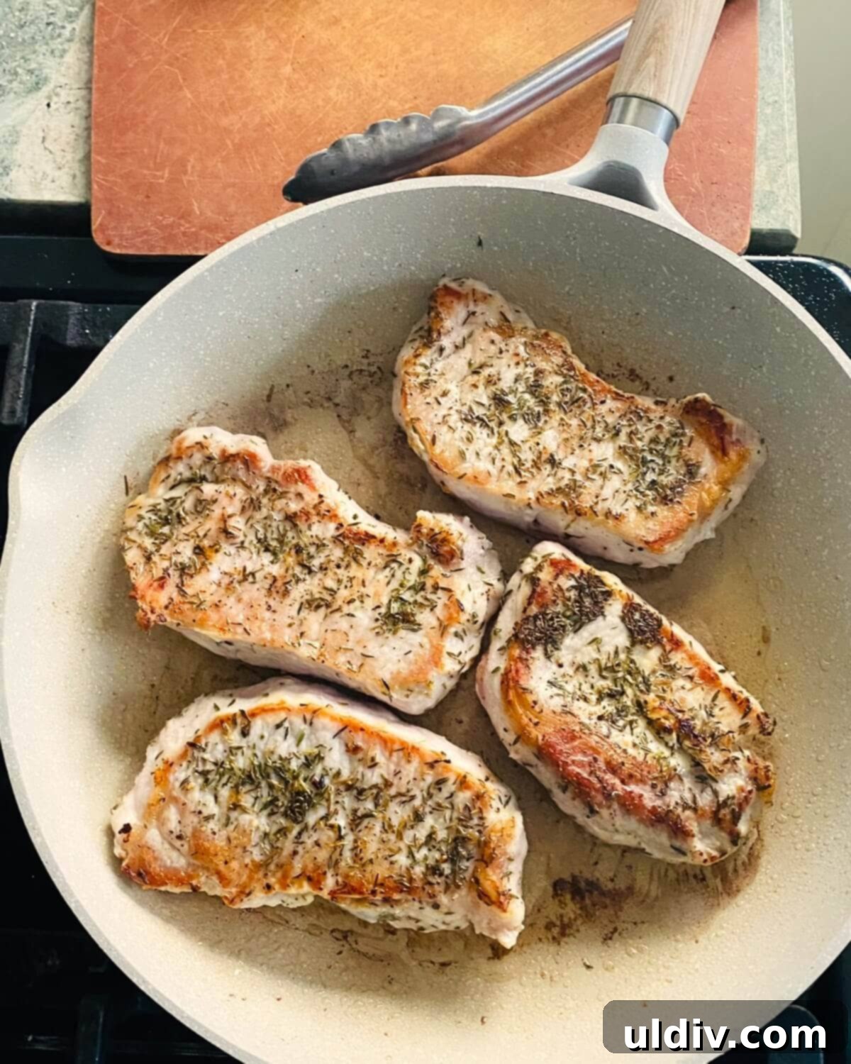 Pork chops sizzling in a hot sauté pan, achieving a golden-brown crust, indicating proper searing technique.