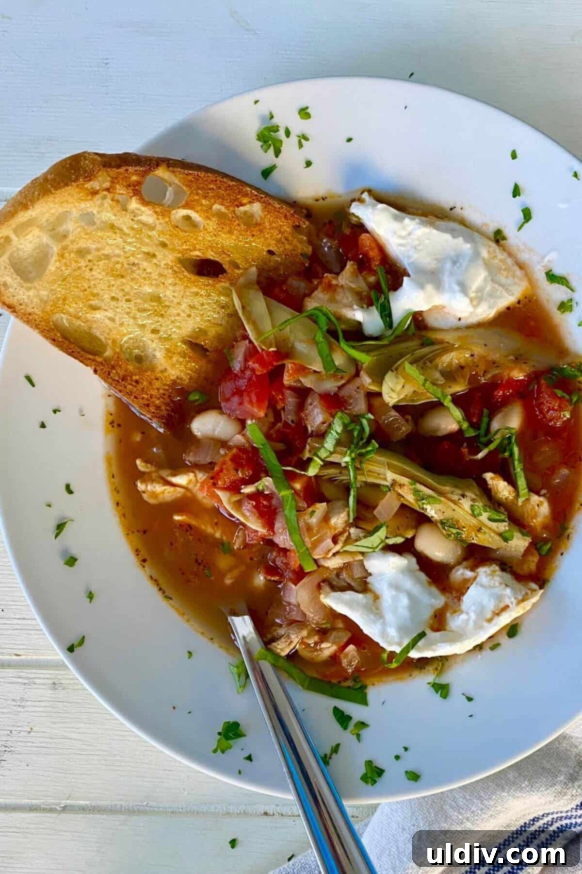 Tuscan Chicken Artichoke Soup 2 A vibrant bowl of Italian chicken soup featuring tender chicken, artichoke hearts, cannellini beans, and a swirl of creamy burrata, garnished with fresh basil.