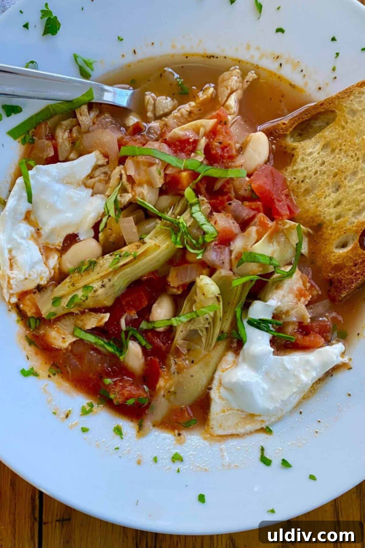 Tuscan Chicken Artichoke Soup 8 A generously filled bowl of hearty Italian chicken soup, garnished with fresh basil leaves and a dollop of creamy burrata, showcasing the tender chicken, artichokes, and beans within the rich tomato broth.