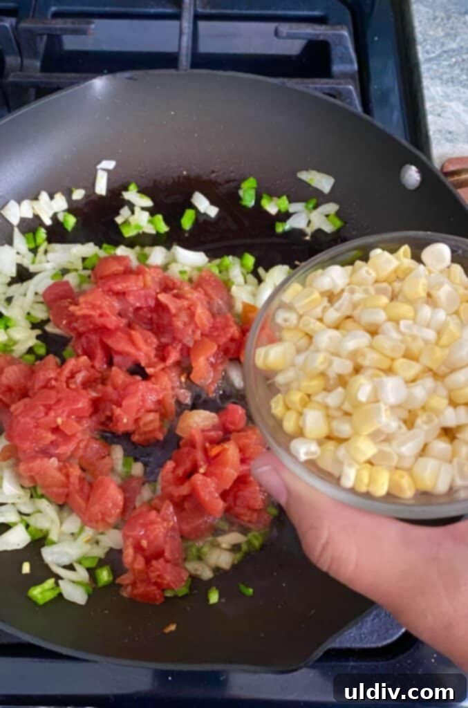 Adding sweet corn to a sauté of tomatoes and other vegetables in a pan, preparing the tortilla stack filling.