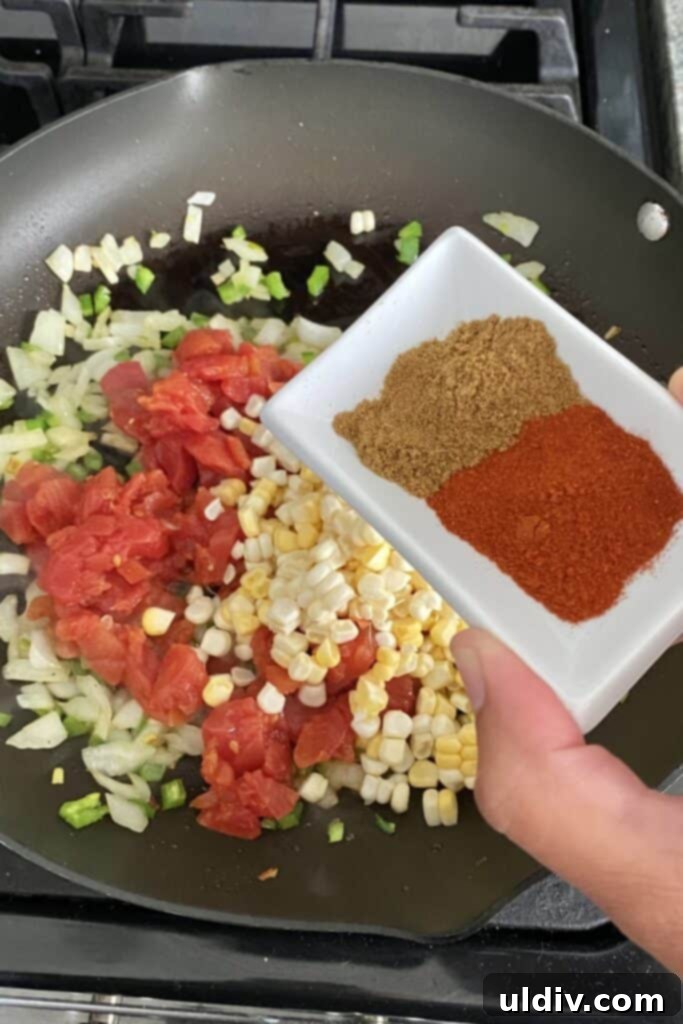 A chef adding Tex-Mex spices, including cumin and smoked paprika, to the simmering vegetable sauté for enhanced flavor.
