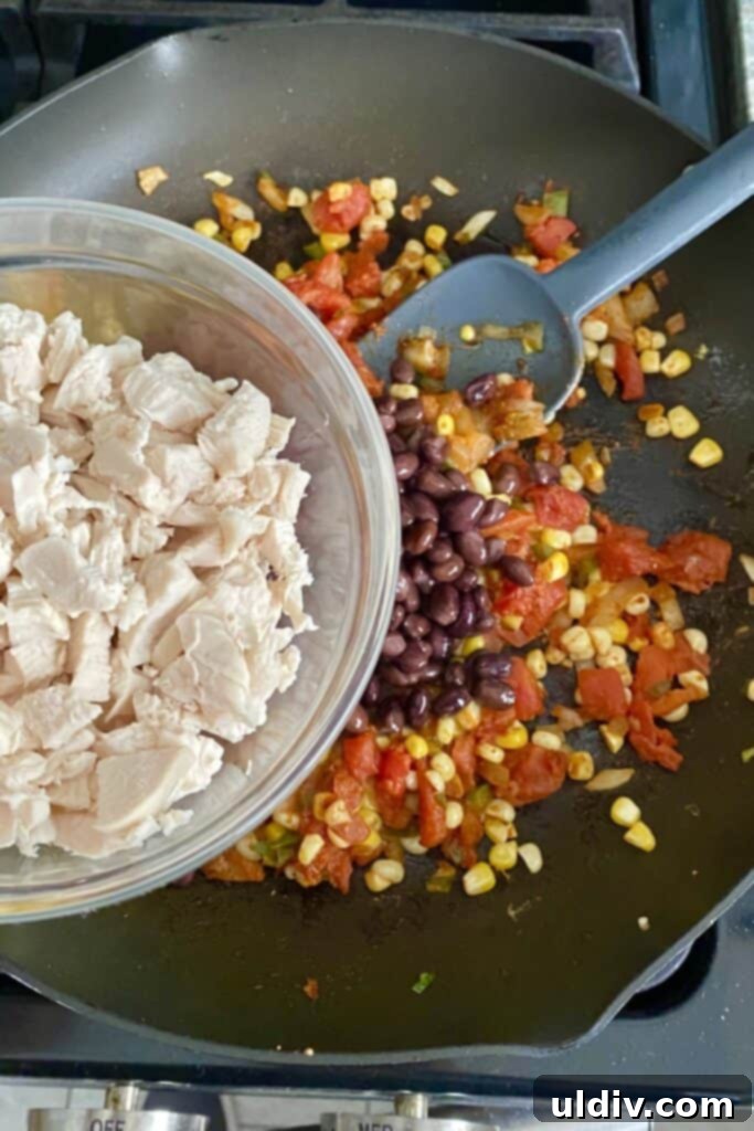 Cooked chicken being incorporated into the flavorful filling mixture for the tortilla stacks, adding protein.