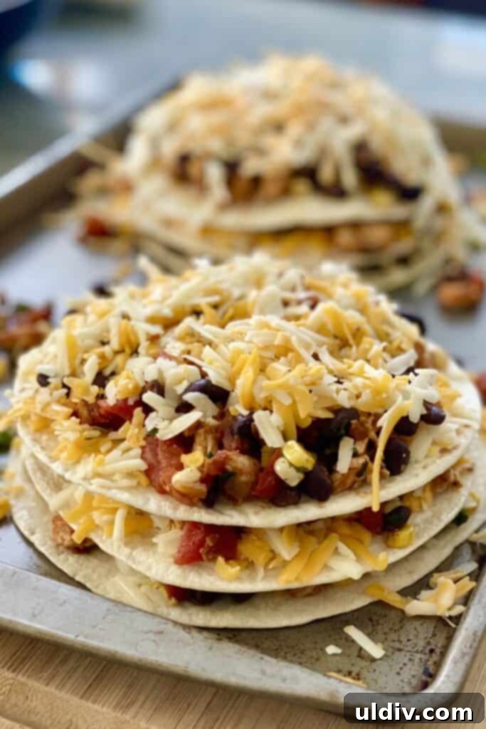 Unbaked tortilla stacks neatly arranged on a baking sheet, ready for the oven, showing the layers of filling and cheese.