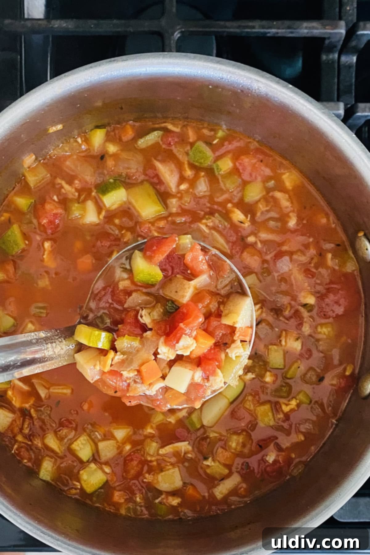 Grandma's Beloved Manhattan Clam Chowder Recipe 7 A ladle full of rich and chunky Manhattan clam chowder, showcasing the vibrant tomato broth and abundant vegetables.