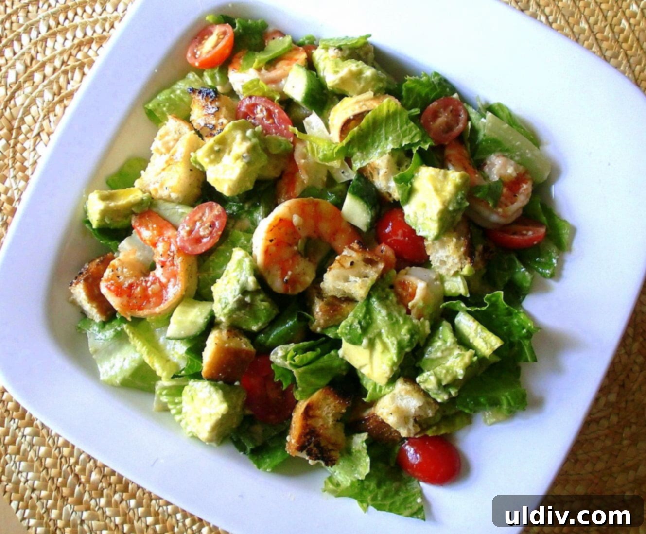 A Caesar salad with grilled shrimp in a white bowl.