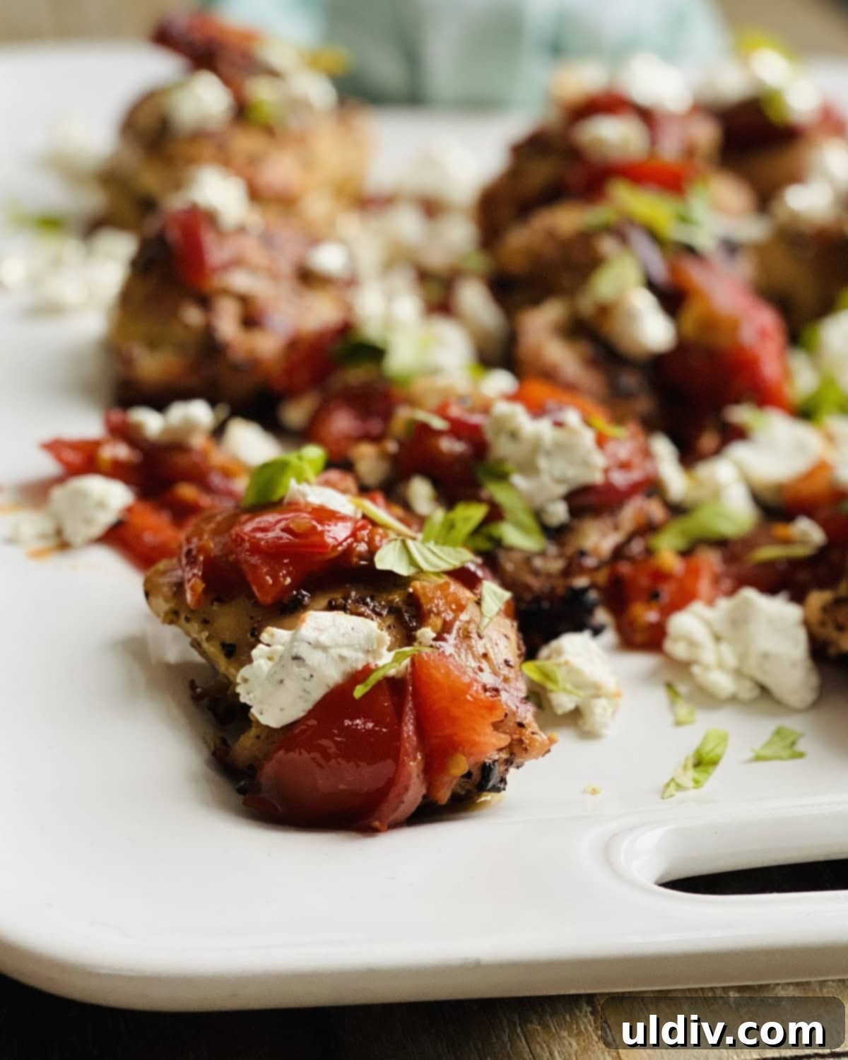 Bruschetta & Goat Cheese Grilled Chicken 9 Closeup of a chicken thigh topped with rich bruschetta and soft goat cheese crumbles, garnished with basil