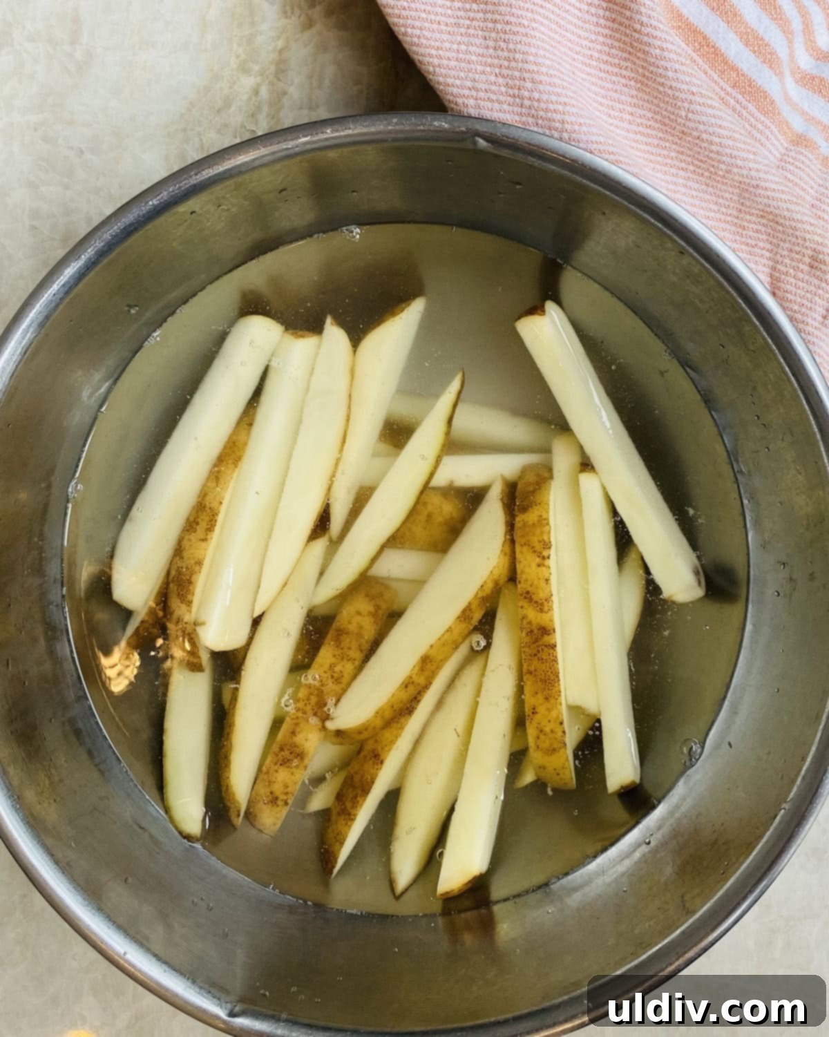 Homemade Crispy Oven Fries 5 Freshly cut potato sticks soaking in a large bowl of cold water.