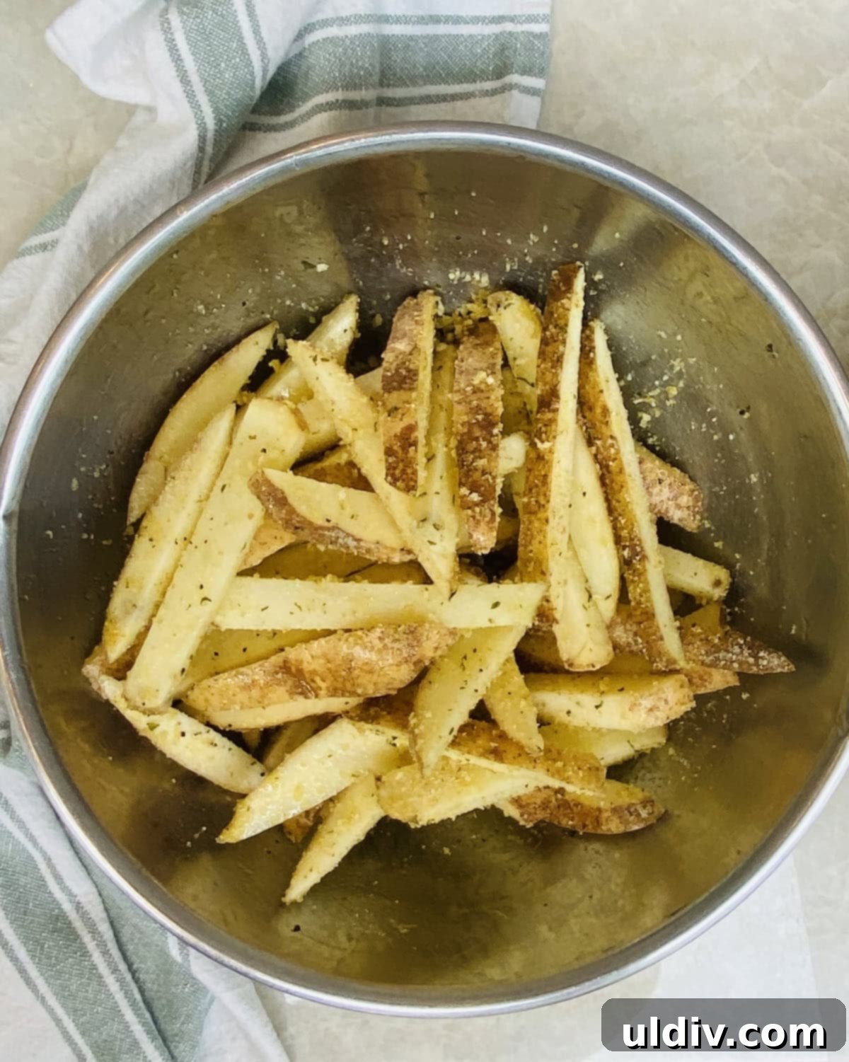 Homemade Crispy Oven Fries 7 A large bowl filled with dry cut potatoes, drizzled with olive oil and seasoned with panko, salt, and pepper, ready for tossing.