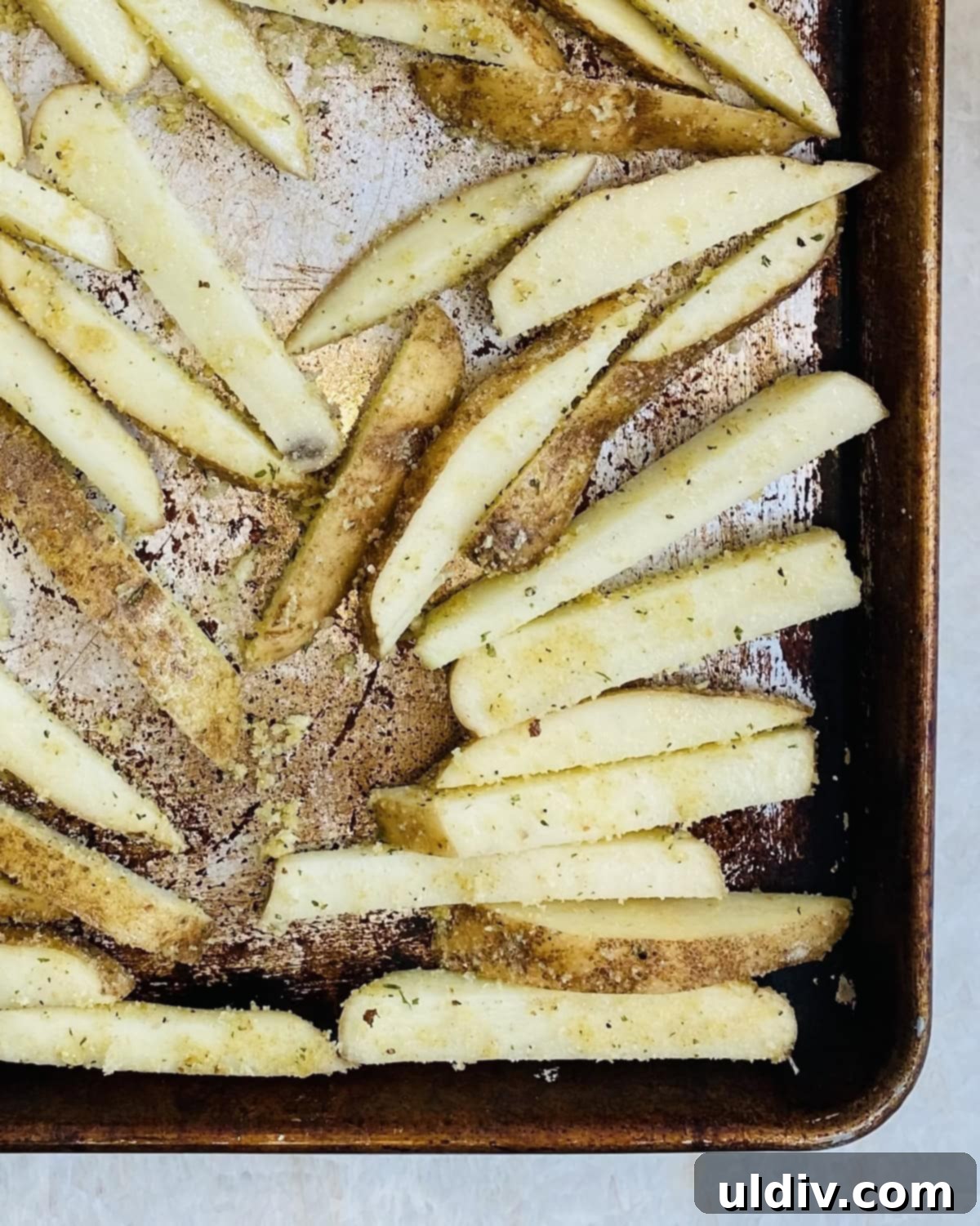 Homemade Crispy Oven Fries 8 An unbaked baking sheet with seasoned oven French fries spread in a single layer, ensuring no pieces are touching.