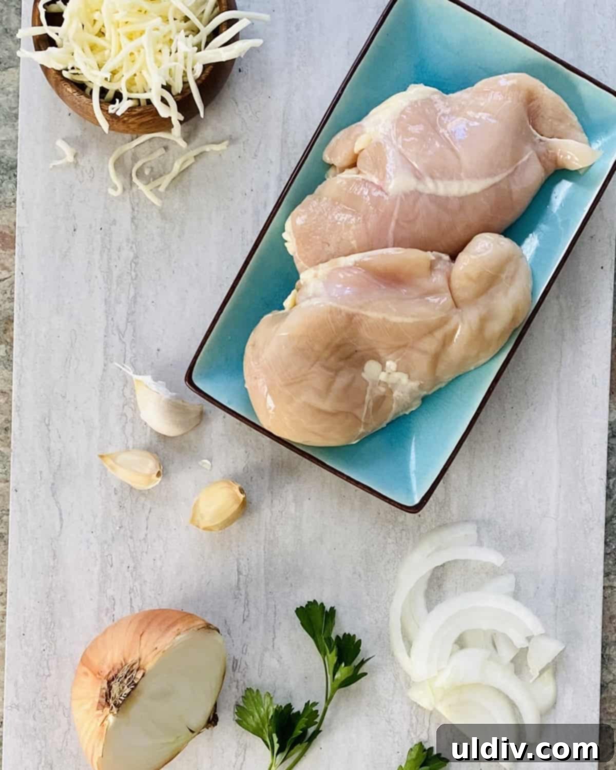 Classic French Onion Chicken Bake 3 Ingredients for French Onion Chicken Bake laid out: chicken breasts, fresh parsley, mozzarella cheese, onion, garlic.